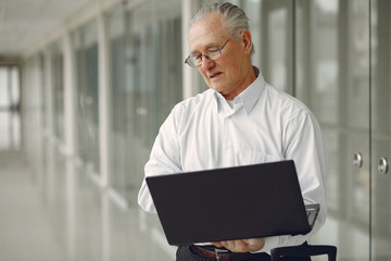 Man in the office. Old man use the laptop. Senior in a white shirt.