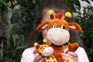 The girl holds a soft toy giraffe in front of her face. The concept of childhood.