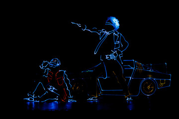 Silhouettes of dancing people in luminous costumes on a black background. LED suit.