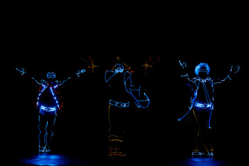 Silhouettes of dancing people in luminous costumes on a black background. LED suit.
