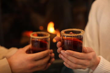 Couple with mulled wine near fireplace indoors, closeup. Winter vacation