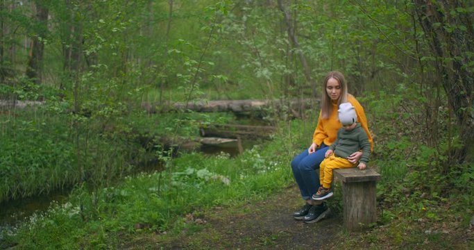 Mother and son sitting on a log of a tree in the forest near the stream talking and pointing ahead. Look ahead. To consider and explore. Mother tells her son and introduces him to nature.