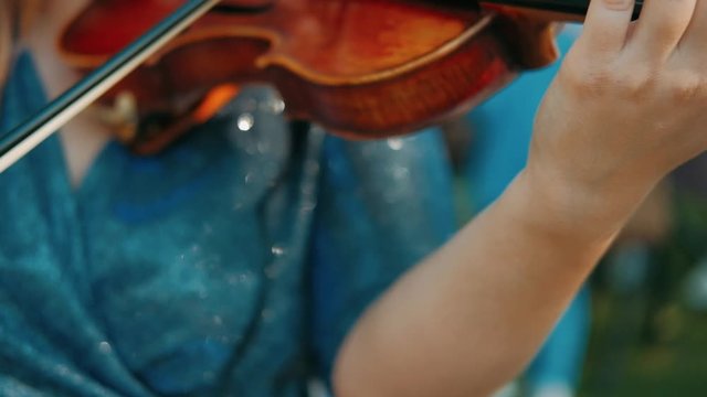 Girl violinist playing the violin outdoors. Green leaves backgound. Close up. Musician playing. Slow motion.