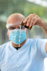 Doctor wearing a surgical mask and medical safety goggles emptying a bottle of expired liquid...