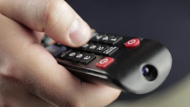 man holding a remote control pressing different buttons and switching channels of tv