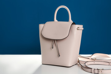 Stylish woman's bag on white table against blue background