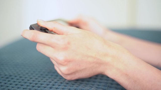 The girl plays on Nintendo Switch lying on the blue bed. Game controller in female hands close-up. A portable game console