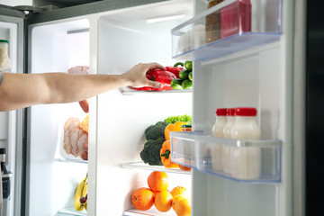 Young man taking bell pepper out of refrigerator, closeup