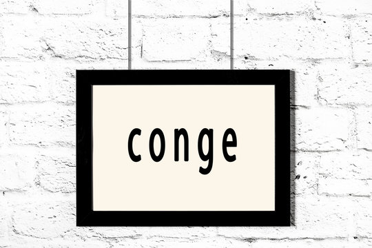 Black frame hanging on white brick wall with inscription conge