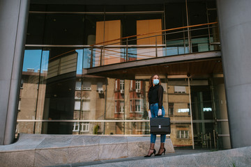 A beautiful attractive caucasian businesswoman with a mask and gloves stands in front of the company. COVID - 19 virus protection