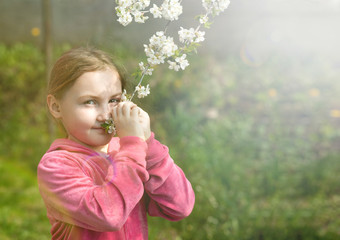 a little girl sniffs a flowering branch of a fruit tree in the spring garden