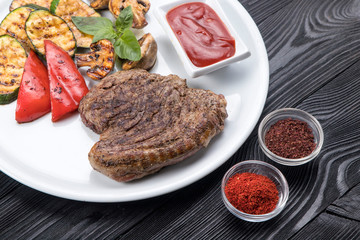 grilled steak, zucchini, on a white plate and black background