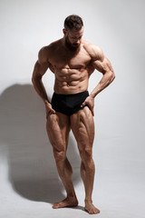 Fototapeta na wymiar Athletic bearded man shows muscles standing in full growth on a light background.