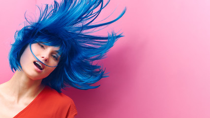 studio portrait of a sexy beautiful girl with a smile in motion on a pink background. Girl with blue hair