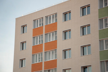 Modern new building with a lot of flats. There are windows and balconies. Light blue sky above
