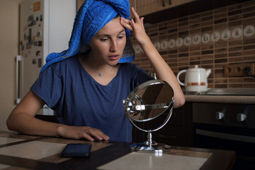 Fototapeta na wymiar Beautiful asian woman wrapped in blue towel sitting on kitchen applying day cream on her forehead, getting ready, morning routine.