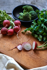 Sliced radish on the wooden board with dill, broccoli and parsley.