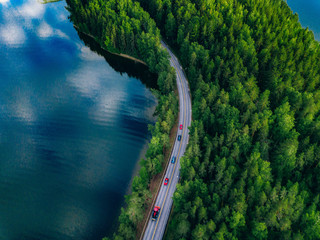 Aerial view of road with cars between green forest and blue lake water in Finland