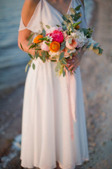 Bride holds wedding bouquet near sea