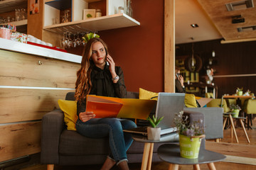 A beautiful caucasian business woman is sitting in a cafe, talking on the phone and working on a laptop. Work in a cafe