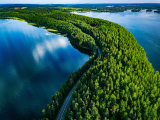 Aerial view of road with cars between green forest and blue lake water in Finland