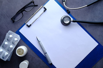 White sheet paper with silver pen, stethoscope and pills on table.