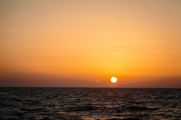 sunset on the beach. View from the water. The sun is sinking below the horizon. Mountains in the background.