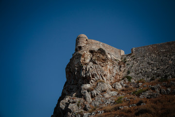 Fototapeta na wymiar Historic stone ancient fortress standing on the edge of a cliff on the island. Blue sky background.