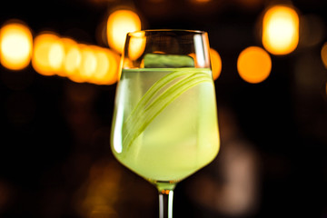 A close-up of a beautiful light green cocktail with celery in a wine glass, bokeh lights, selective focus, horizontal