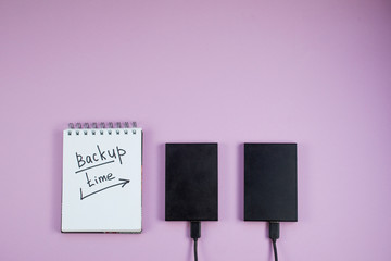 two hard drives and a Notepad with text backup time lie on a lilac background. The view from the...