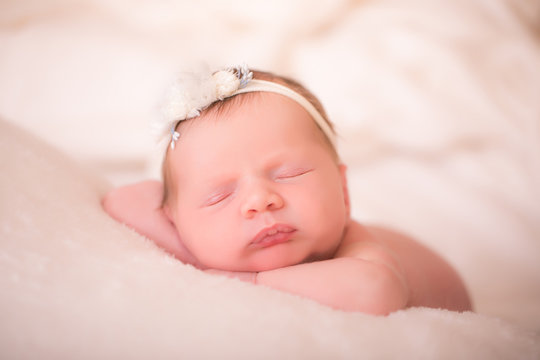 Newborn baby girl wearing a headband is sleeping on her tummy.