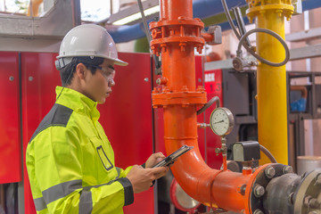 Asian engineer wearing glasses working in the boiler room,maintenance checking technical data of heating system equipment,Thailand people