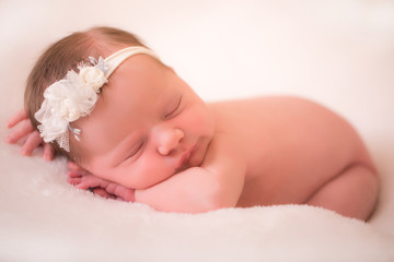 Newborn baby girl wearing a headband is sleeping on her tummy.