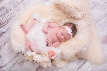 Beatiful newborn girl in floral headband, lying in sleeping basket in blanket.