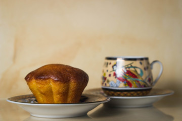 One cupcake and a cup of coffee. Chinese style cup. Photo on a brown background