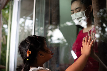Mother wear face mask meeting daughter and touching hand through the window because of the quarantine Corona Virus Covid-19, social distancing
