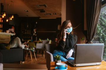 A beautiful caucasian woman with a mask and gloves is sitting in a cafe and using the phone. COVID virus protection - 19
