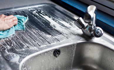 Cleaning the kichen sink with brush and cloth.
