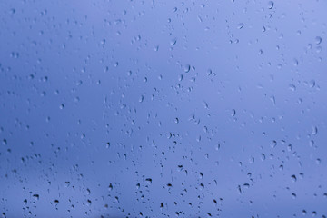 blue abstract background from drops of water on glass in the evening, selective focus