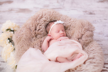 Beatiful newborn girl in floral headband, lying in sleeping basket with flowers on blanket