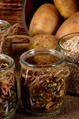 barley, spices in glass jars next to dried mushrooms and raw potatoes on a wooden brown table