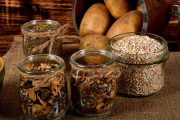 barley, spices in glass jars next to dried mushrooms and raw potatoes on a wooden brown table