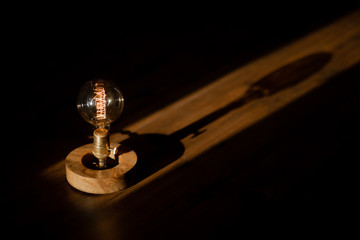 Filament Vintage Bulb with knob and wooden base over dark background clicked during golden hour with light & shadow play.
