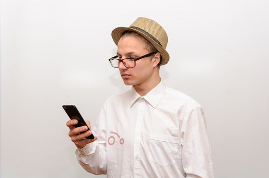 A young man with glasses and a hat is looking at his cell phone.