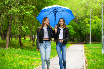 Two happy girlfriends walk in the park in rainy weather