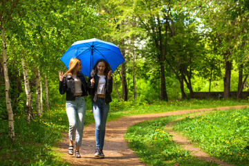 Fototapeta premium Two happy girlfriends walk in the park in rainy weather
