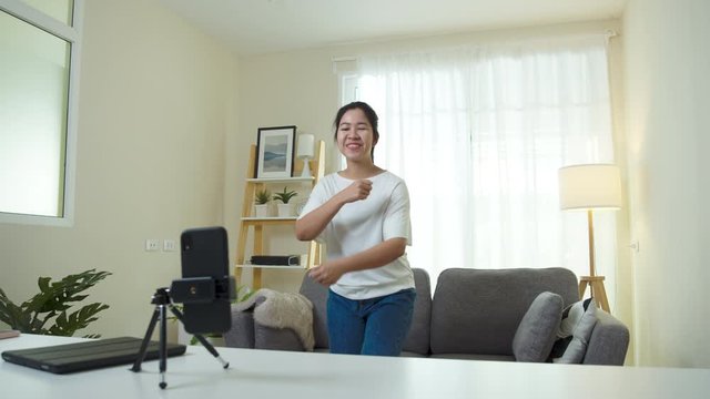 Asian woman creating short video by mobile application online service. Cute girl happy, enjoy and dance for sharing content to social media.Home entertainment online during quarantine from coronavirus