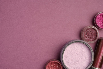 Glitters, lipsticks, lip glosses, shadows and powder in lilac colors stand on a plum background from the right edge of the frame