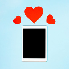 Tablet on a blue background with cute hearts. The concept of meeting website, love in internet, love to your gadget and technology, love correspondence, Valentine's Day, surprise. Flat lay