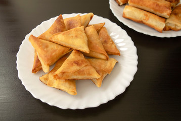 Famous traditional Arabic, Middle East, Asian cuisine. Triangular arabic chicken samosa and spring rolls on dark wooden background. Many mini samosas on white plate